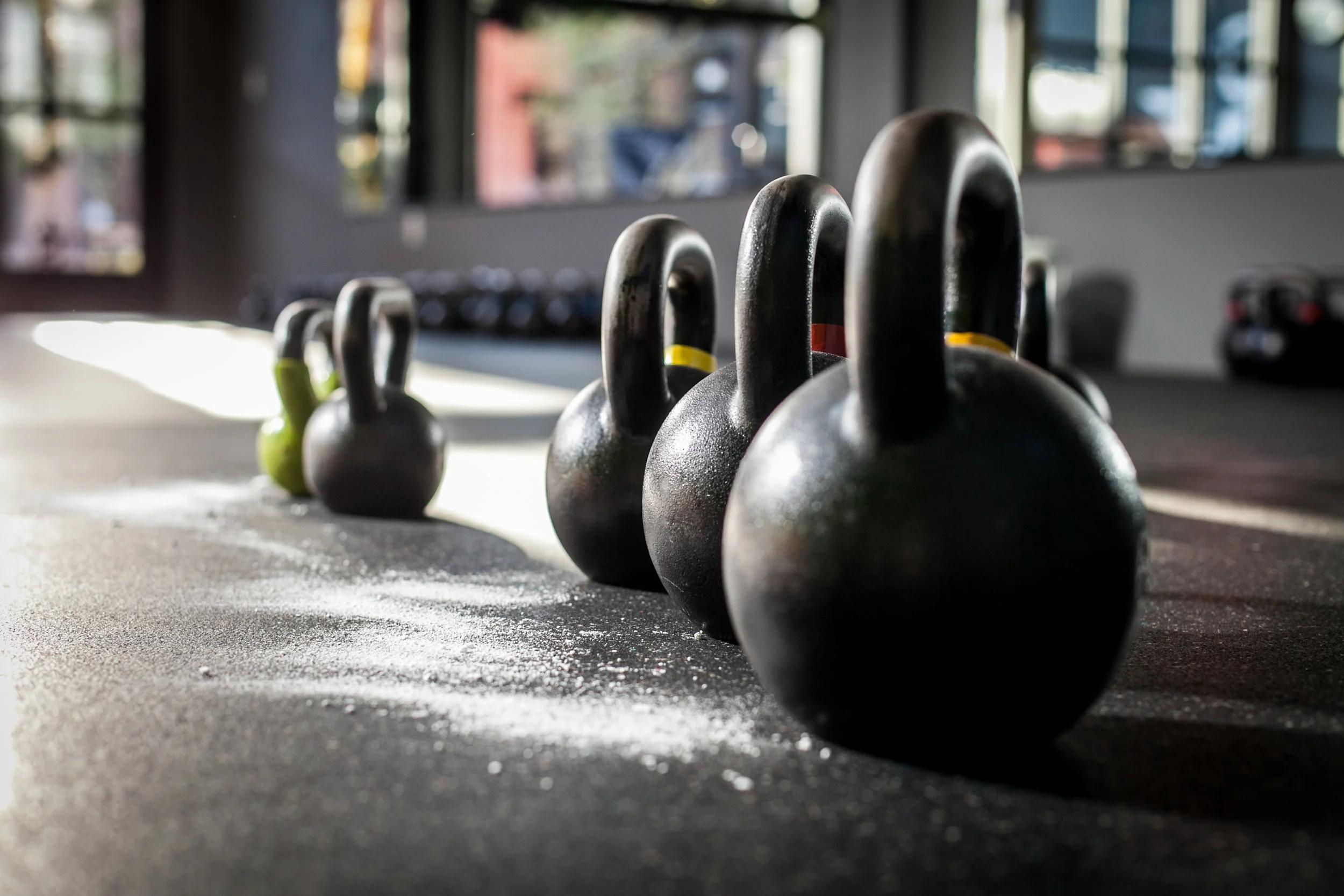 A row of kettlebells of varying sizes lined up on a gym floor.