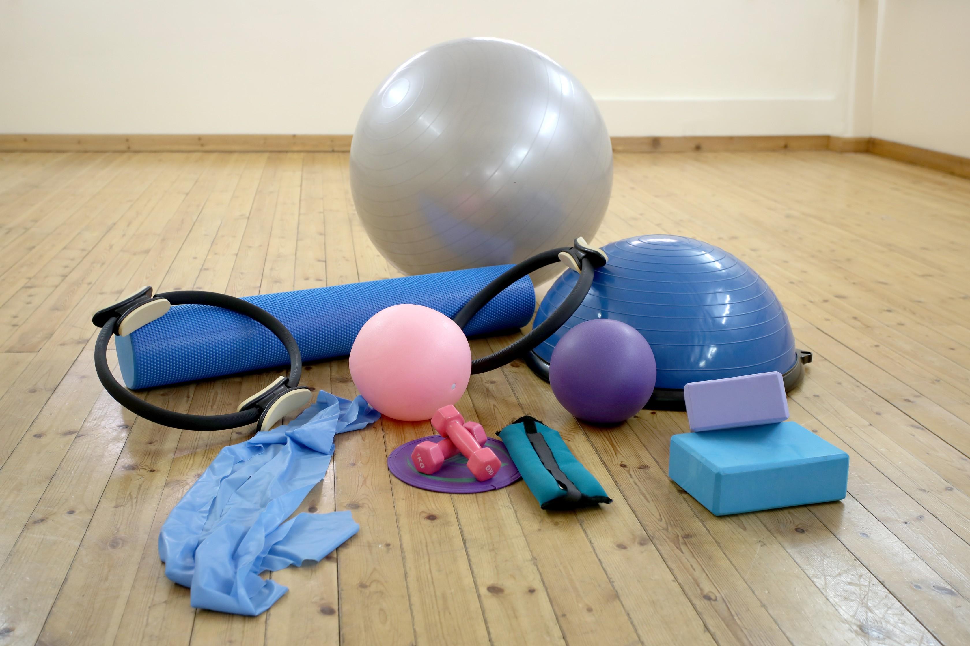 A collection of yoga and flexibility accessories laid out on a wooden floor, including a mat, blocks, roller and resistance bands.